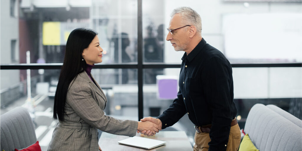 Two businesspeople shake hands in an office setting.