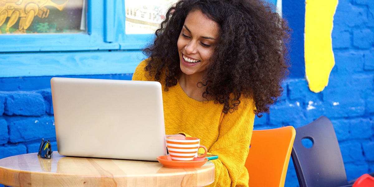 Happy young woman sitting at outdoor cafe using laptop