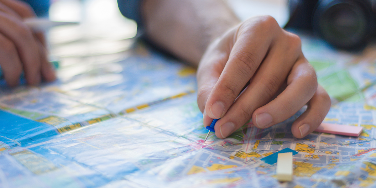 Close-up of hands marking a city map with a blue pencil and sticky notes on a travel planning table.