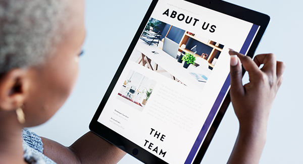 A person holds a tablet displaying an 'About Us' webpage with a photo collage and the 'THE TEAM' section.